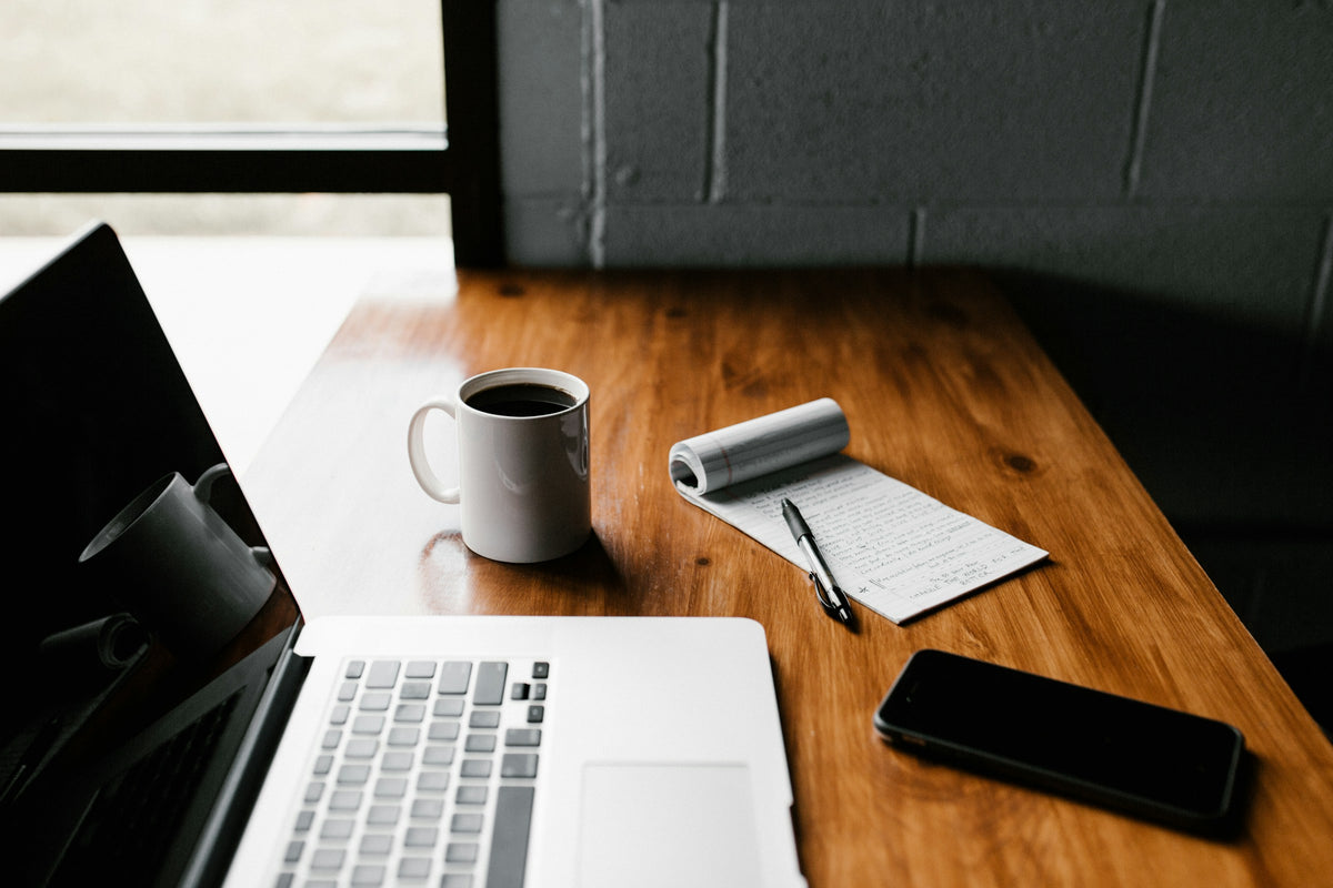 Laptop mit Notizblock und Becher Kaffee