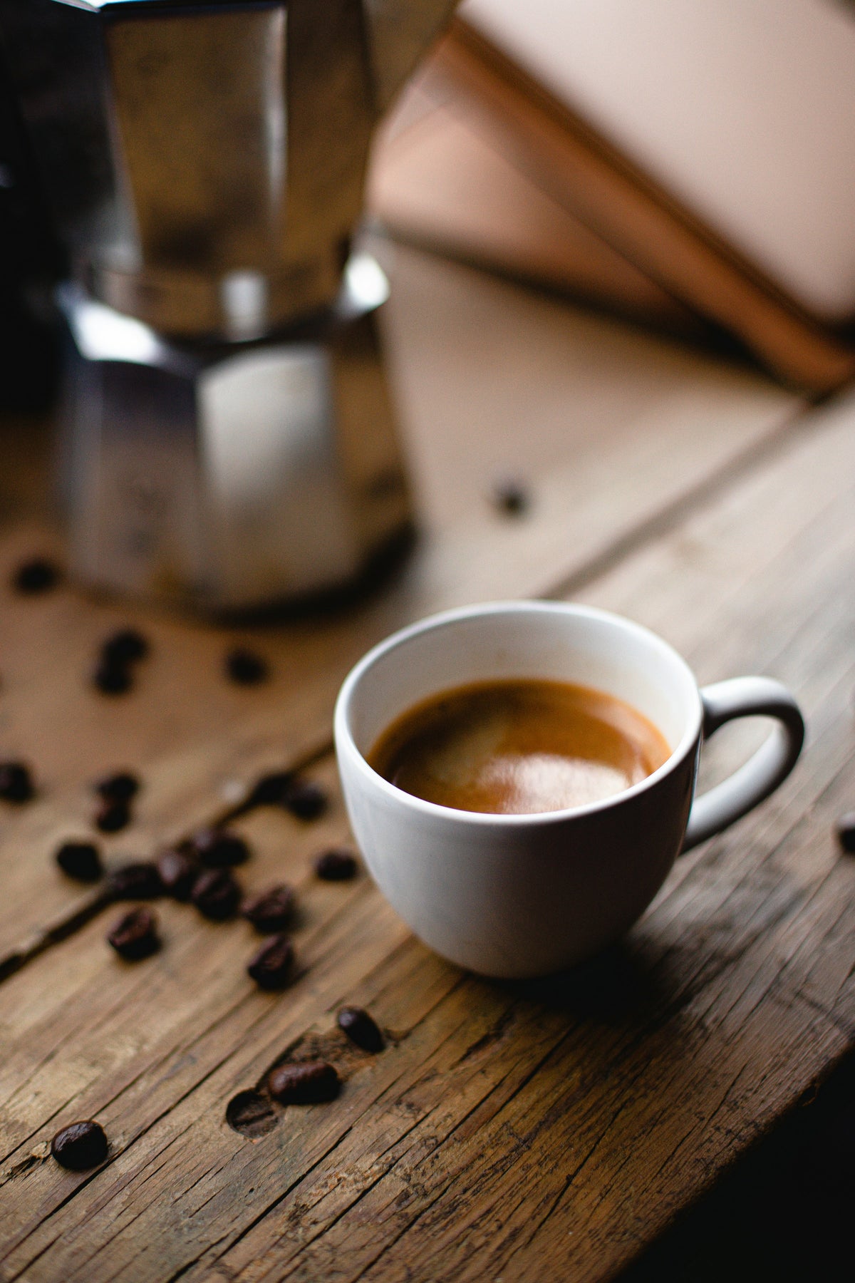Tasse mit Espresso auf Holztisch, mit Espressokocher im Hintergrund