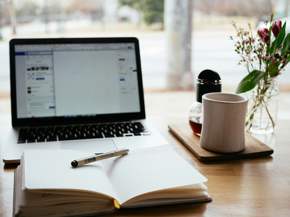 Aufgeklappter Laptop mit Notizbuch und Kaffeetasse